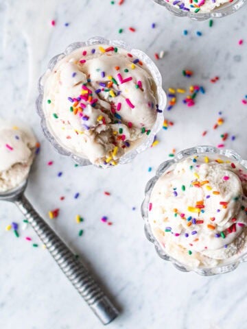 two glass bowls of birthday cake ice cream with sprinkles and ice cream scoop
