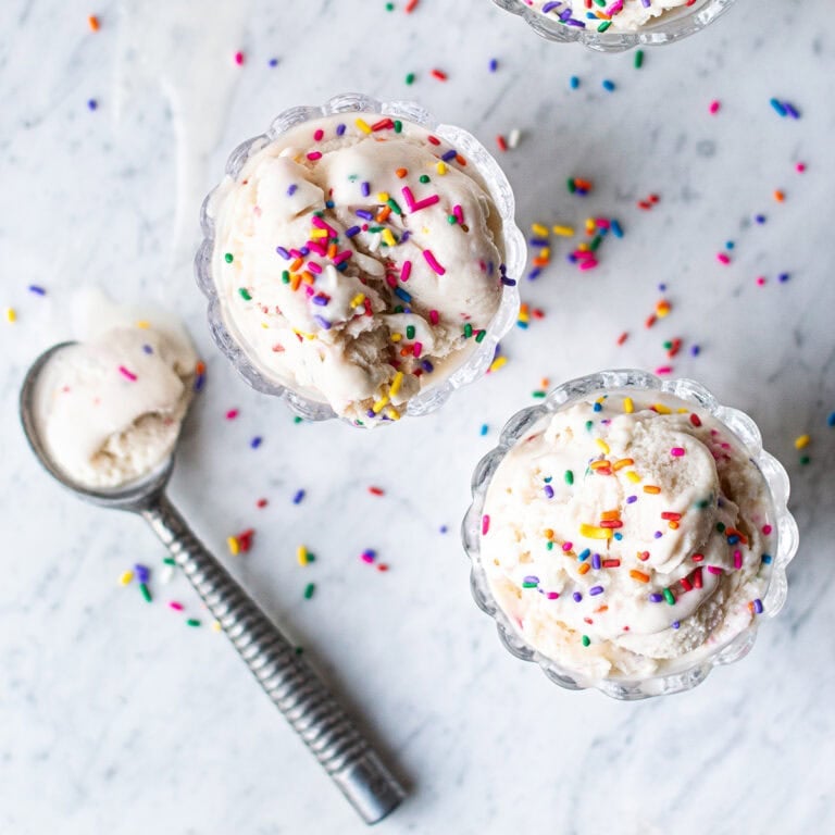 two glass bowls of birthday cake ice cream with sprinkles and ice cream scoop