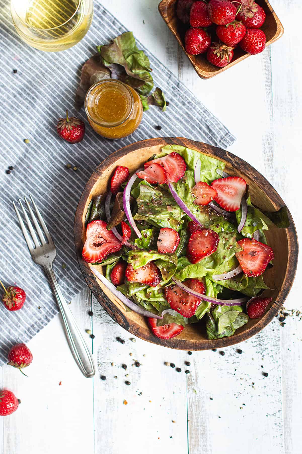 overhead view of strawberry salad with champagne vinaigrette in a wooden bowl, with a jar of dressing and fresh strawberries alongside
