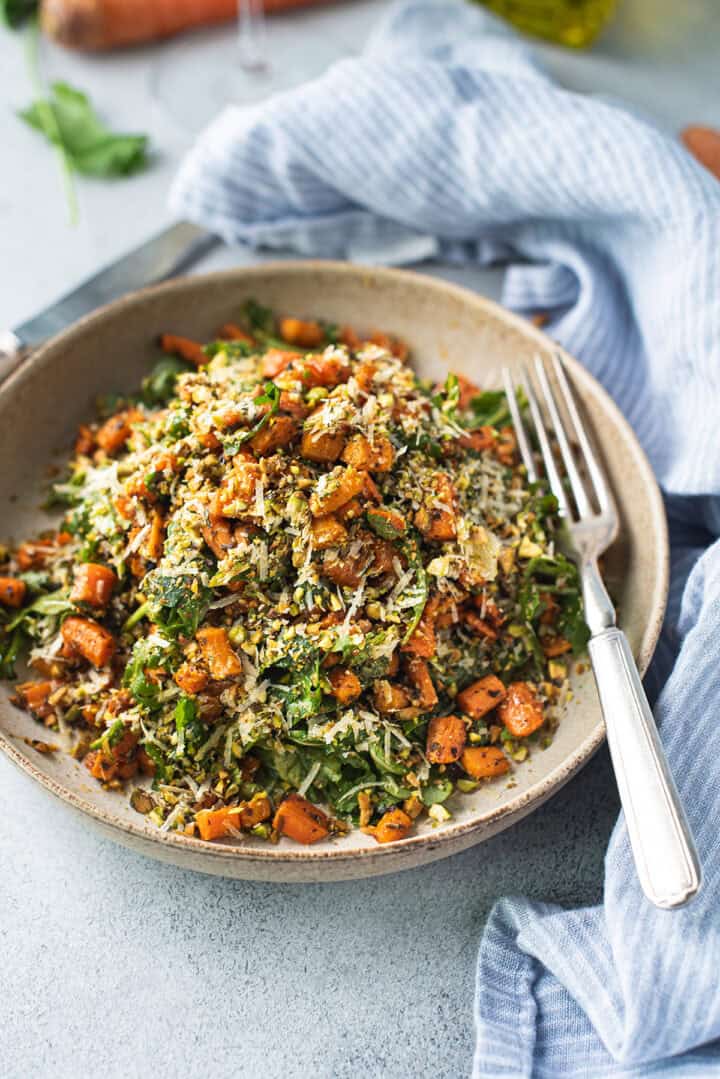 Close up of roasted carrot salad topped with crushed pistachios and shaved parmesan in a ceramic bowl