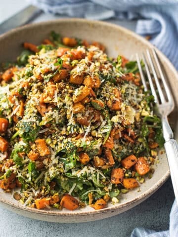 Close up of roasted carrot salad topped with crushed pistachios and shaved parmesan in a ceramic bowl