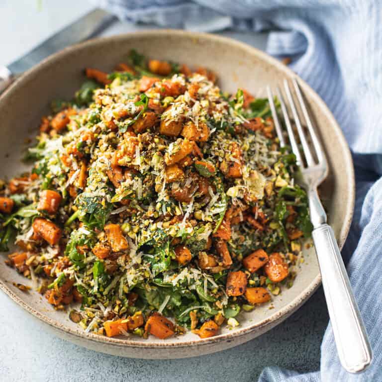 Close up of roasted carrot salad topped with crushed pistachios and shaved parmesan in a ceramic bowl