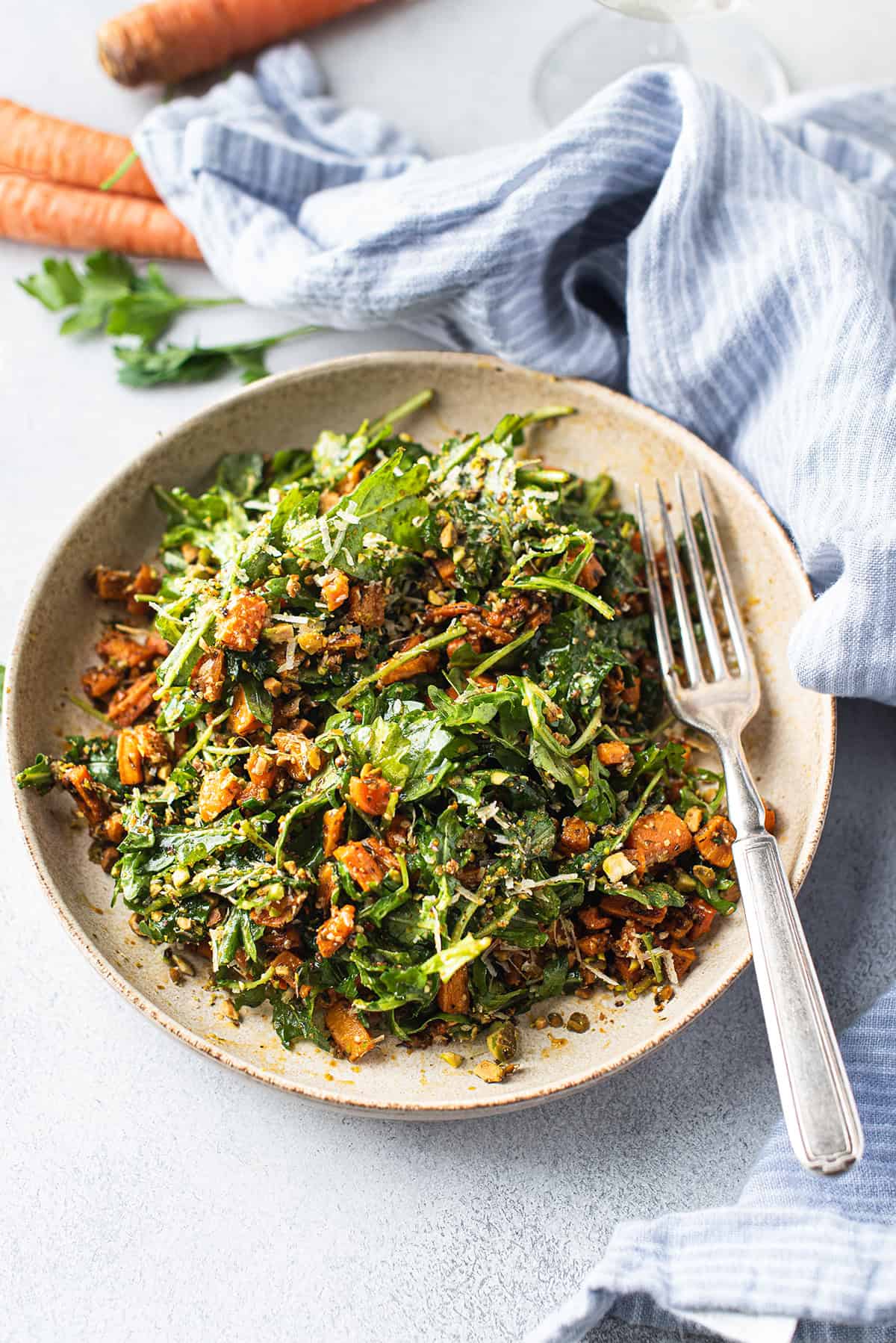 Overhead view of a roasted carrot salad with arugula, pistachios, and shaved parmesan in a rustic ceramic bowl