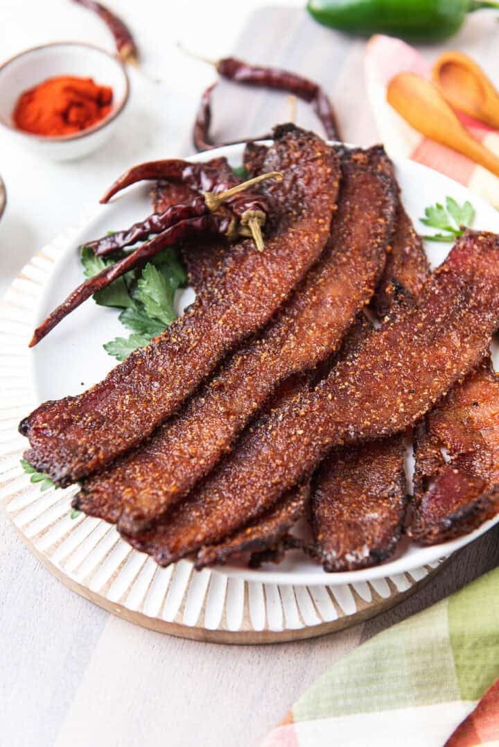 candied bacon strips fanned on a white plate with dried chiles and paprika