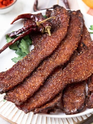 candied bacon strips fanned out on a white plate with dried chiles and paprika