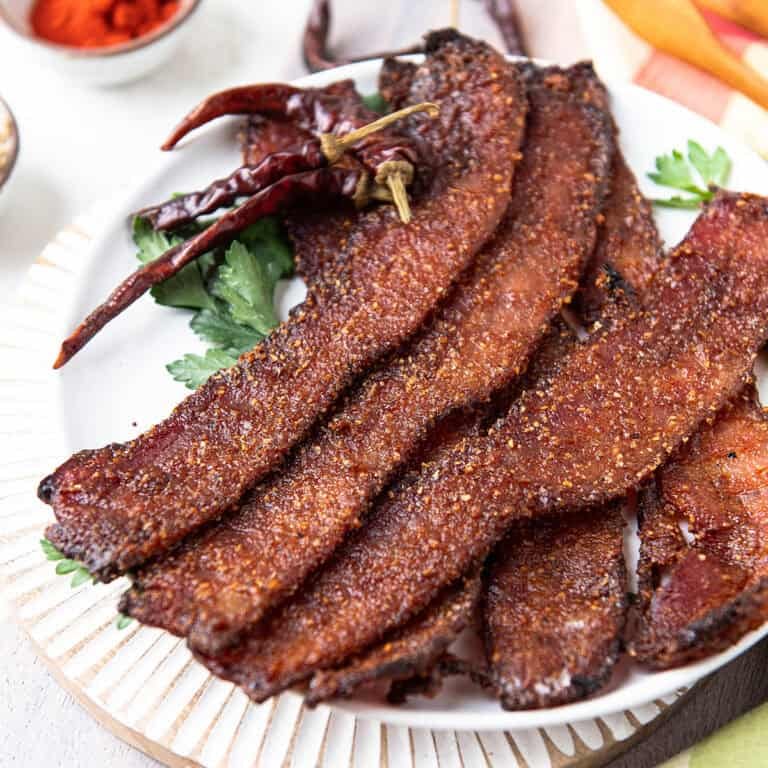 candied bacon strips fanned out on a white plate with dried chiles and paprika