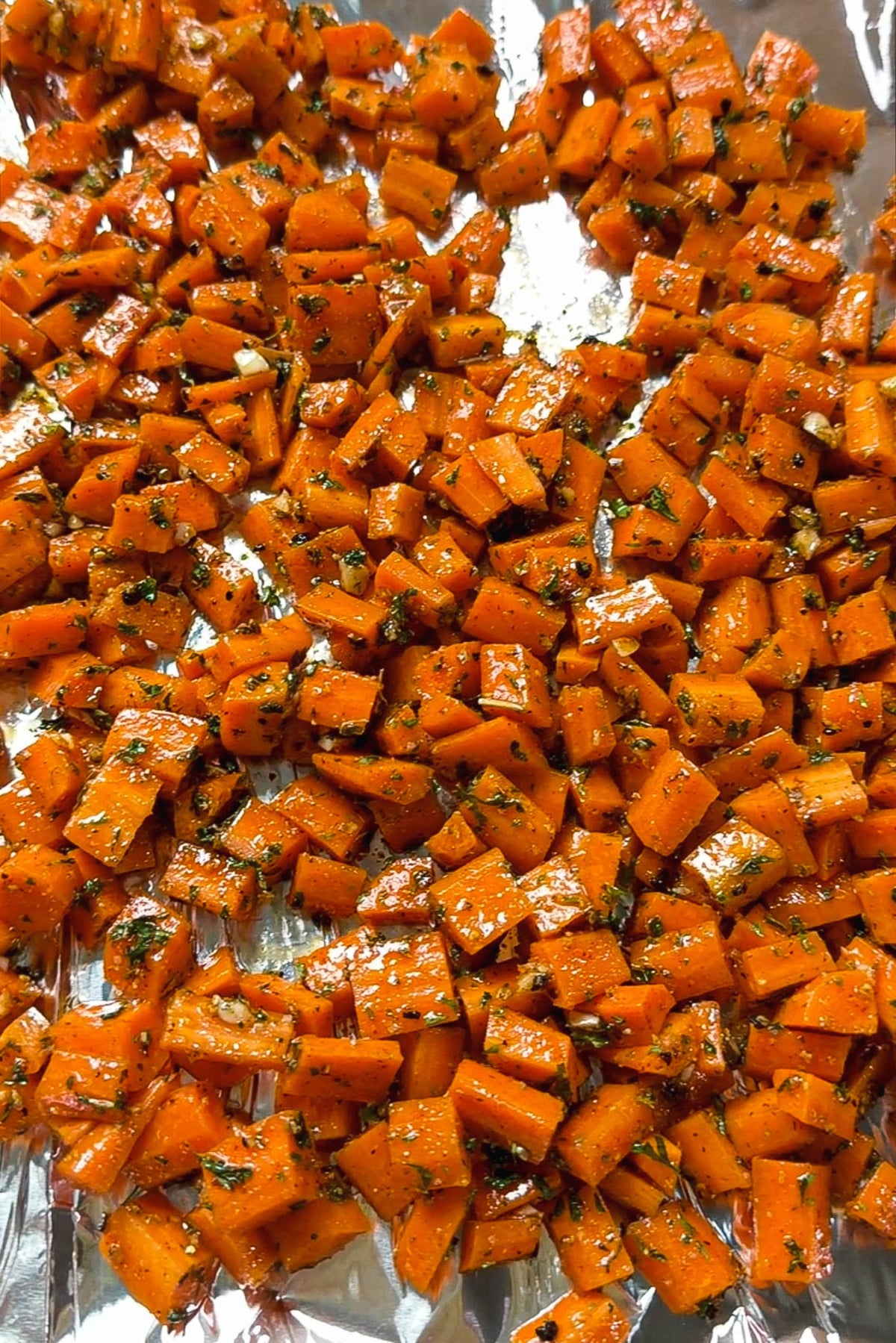 Diced carrots seasoned with smoked paprika and herbs spread in a single layer on a foil lined baking sheet