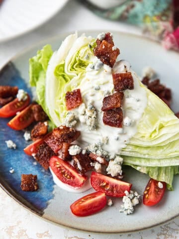 wedge salad plated with iceberg lettuce, blue cheese crumbles, tomatoes, and candied bacon