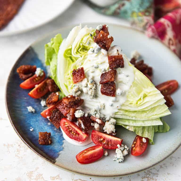 wedge salad plated with iceberg lettuce, blue cheese crumbles, tomatoes, and candied bacon