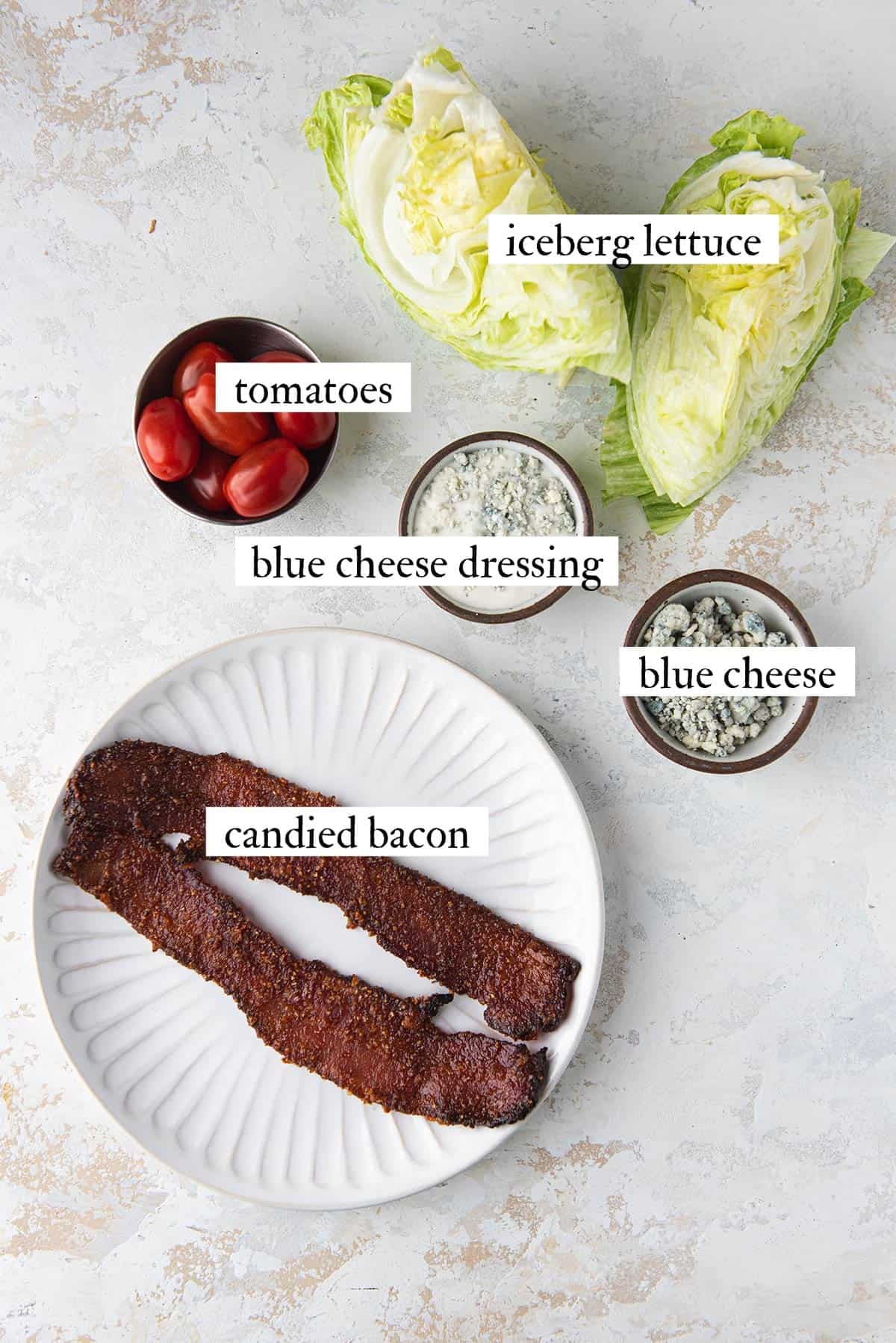 ingredients for wedge salad including iceberg lettuce, blue cheese dressing, blue cheese, tomatoes, and candied bacon