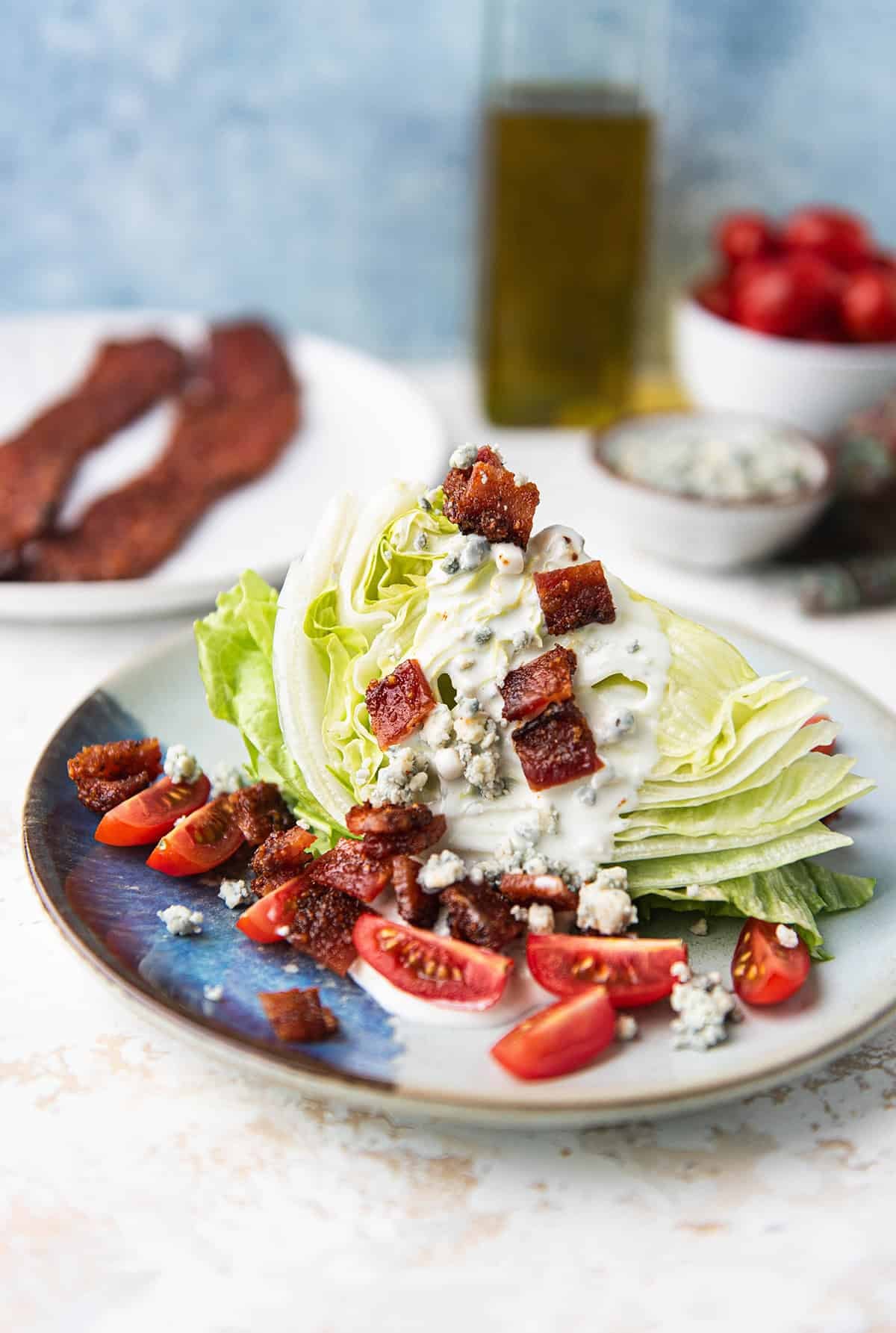 wedge salad plated with iceberg lettuce, blue cheese crumbles, tomatoes, and candied bacon